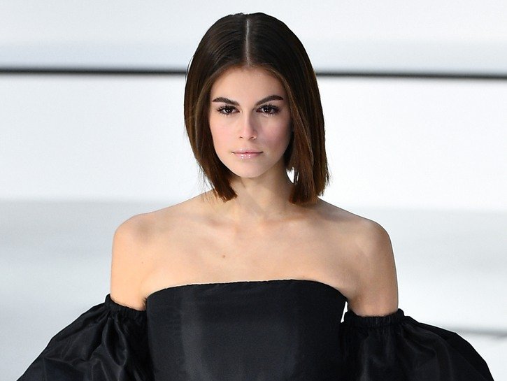 Kaia Gerber in a black dress on a modeling runway.
