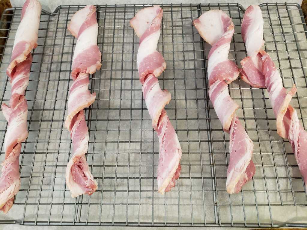 Image of raw bacon twisted and placed along cooling rack.