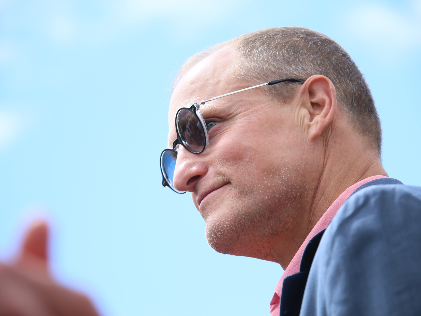Woody Harrelson wearing sunglasses and blue jacket
