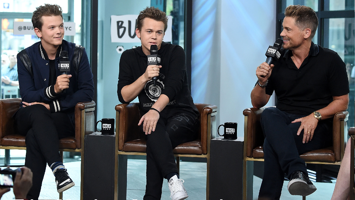 Rob Lowe and his sons John and Matthew wear black tops and bottoms during an indoor event