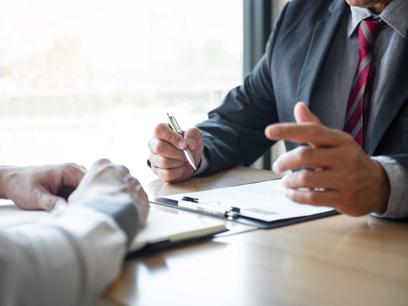 Two men in suits sit at a desk while a job interview is being conducted