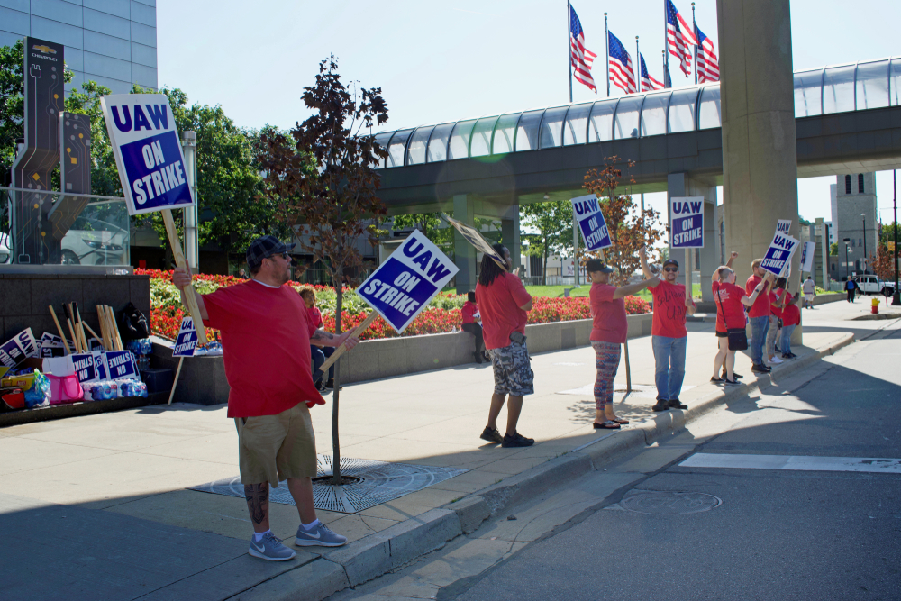 Workers on labor strike hold signs by side of road