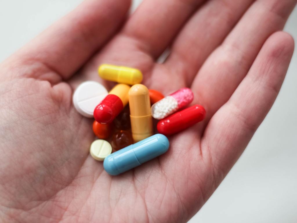 A close up of a hand holding a variety of different vitamins and supplements