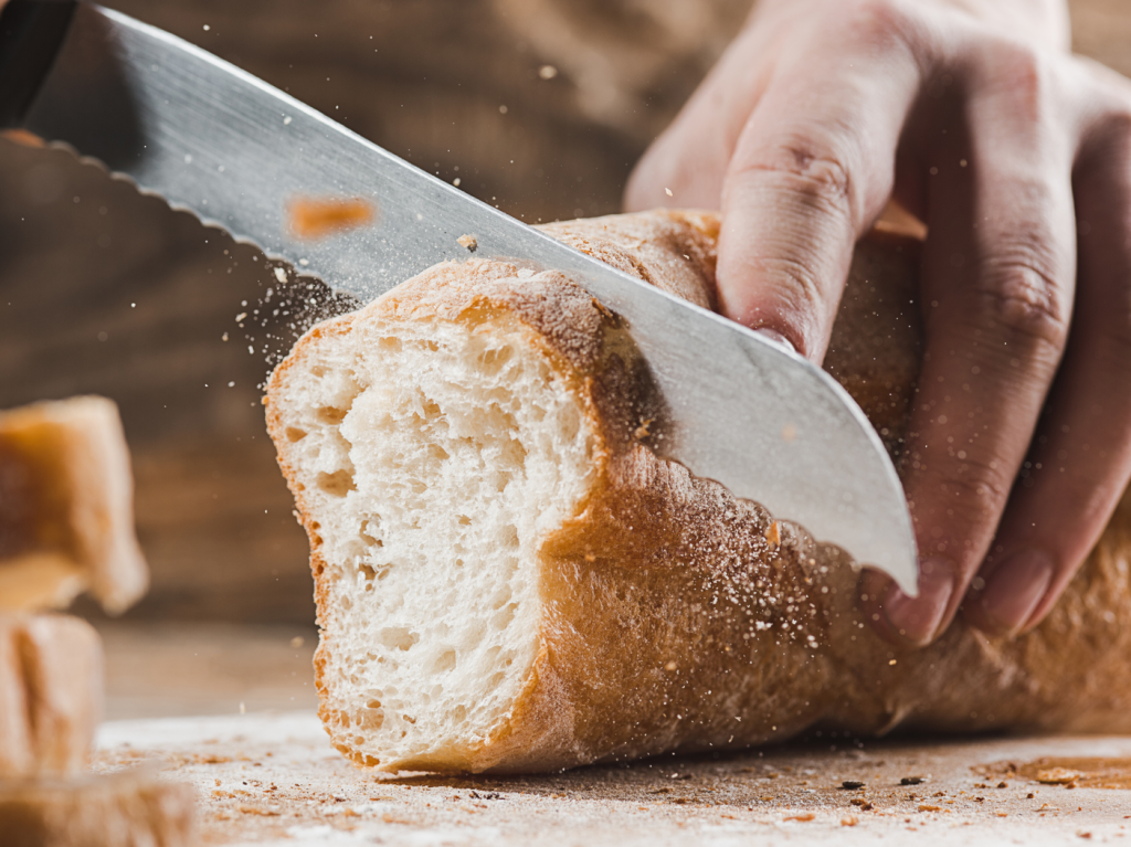 Whole grain bread put on kitchen wood plate with a chef holding gold knife for cut. Fresh bread on table close-up.