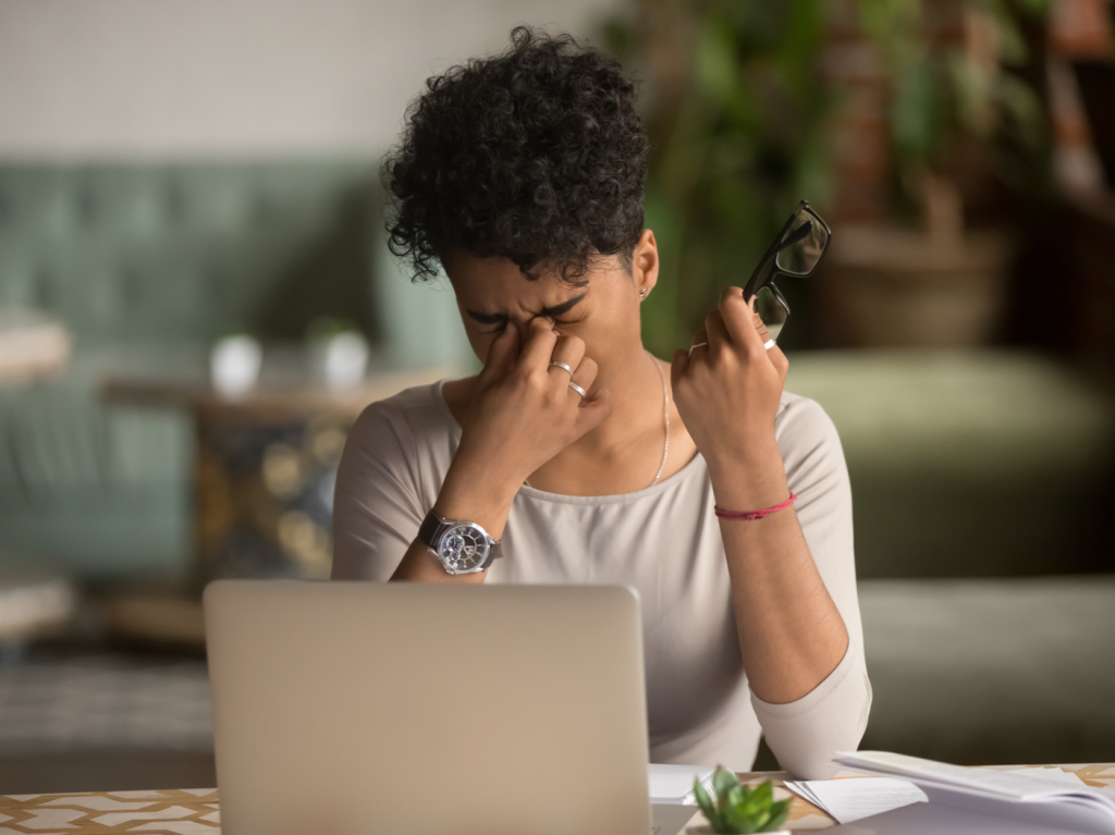 Overworked woman sitting in front of a laptop screen and rubbing her eyes.