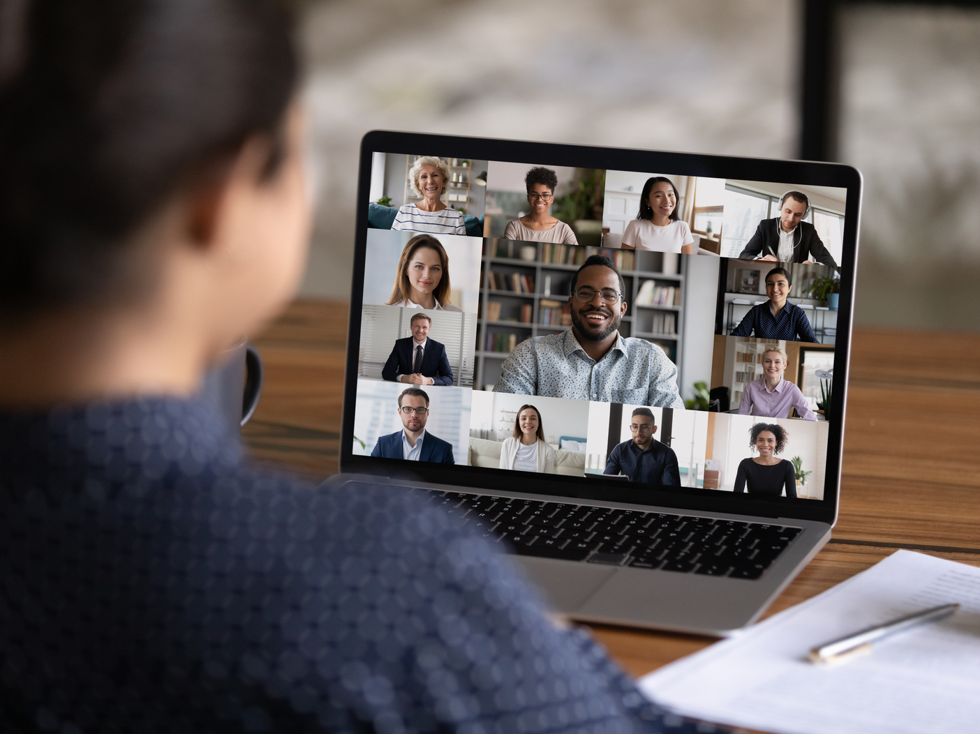 Over shoulder view of female worker have webcam digital virtual conference with diverse multiethnic colleagues. Woman speak talk on video call with multiracial businesspeople.