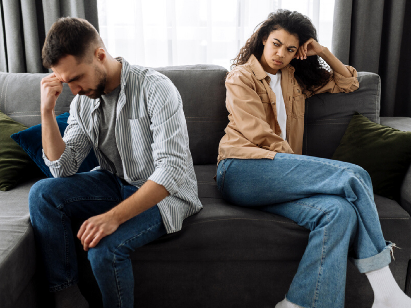 Man and woman sitting on couch, woman looking angrily at man whose head is in his hands