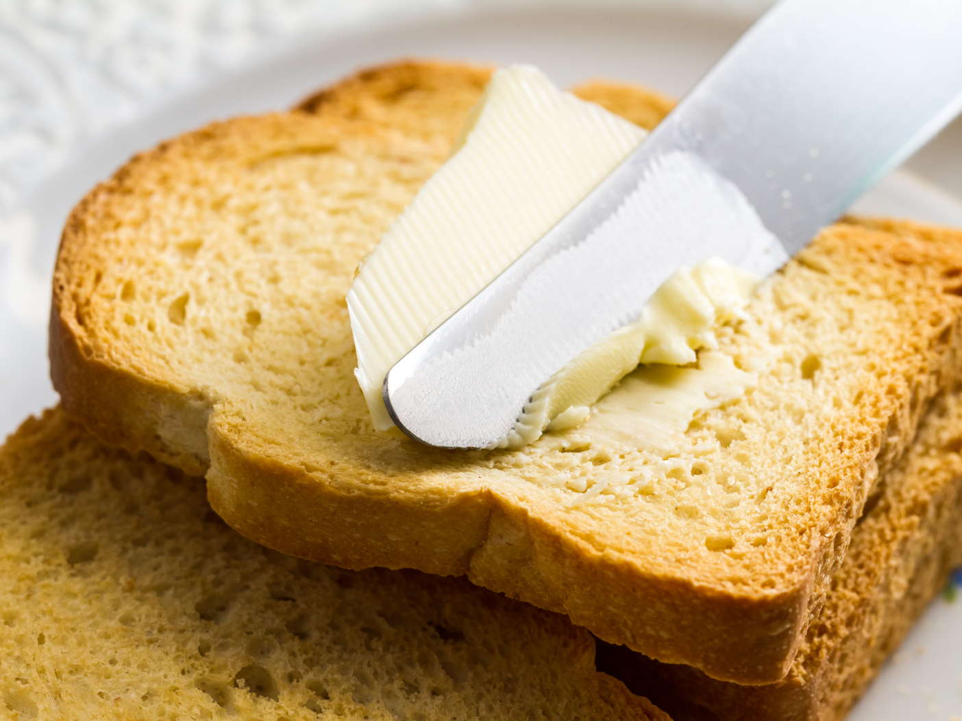 Spreading butter with a knife on sliced brown bread.