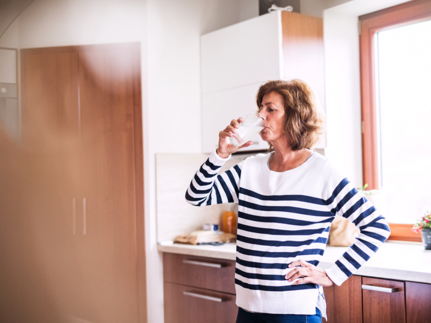 Woman drinking water from a glass in her kitchen.