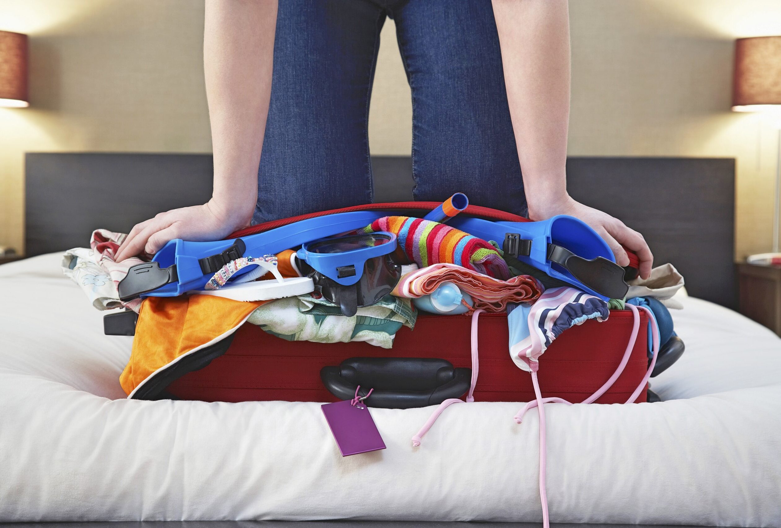 Person kneeling on overpacked luggage trying to zip it shut