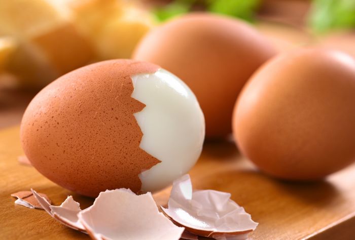 One half-peeled hard-boiled egg with two whole eggs in the background.