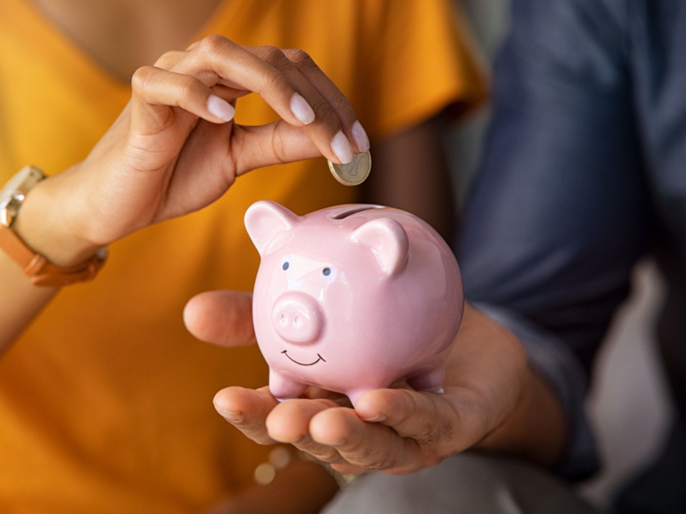 Couple with piggy bank, one partner puts in coin as the other holds it