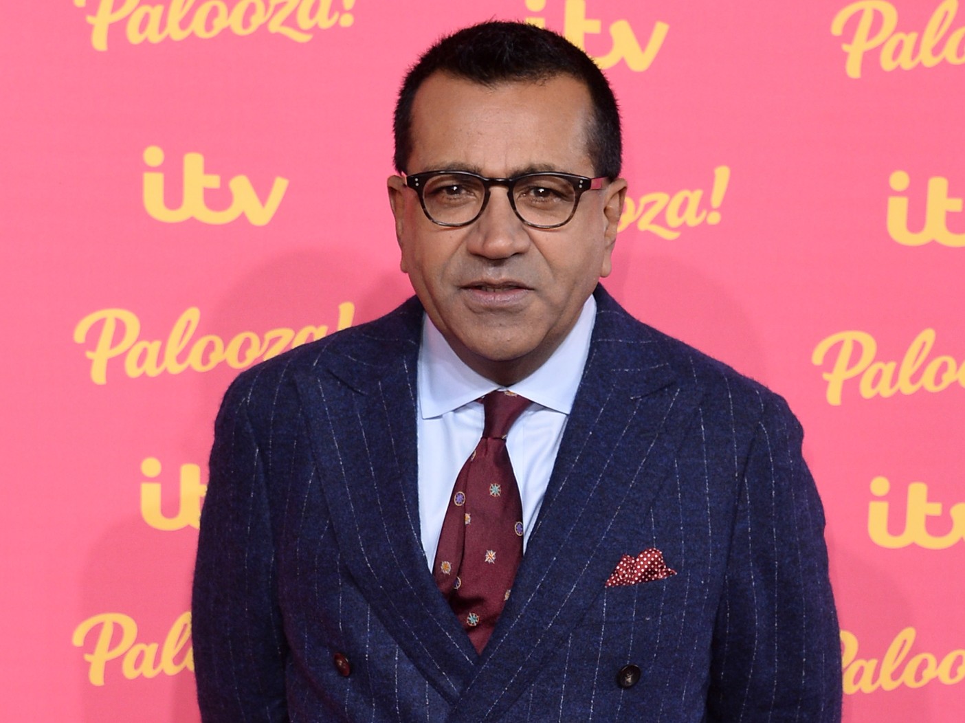 Martin Bashir stands in navy blue suit with burgundy tie against bright pink backdrop