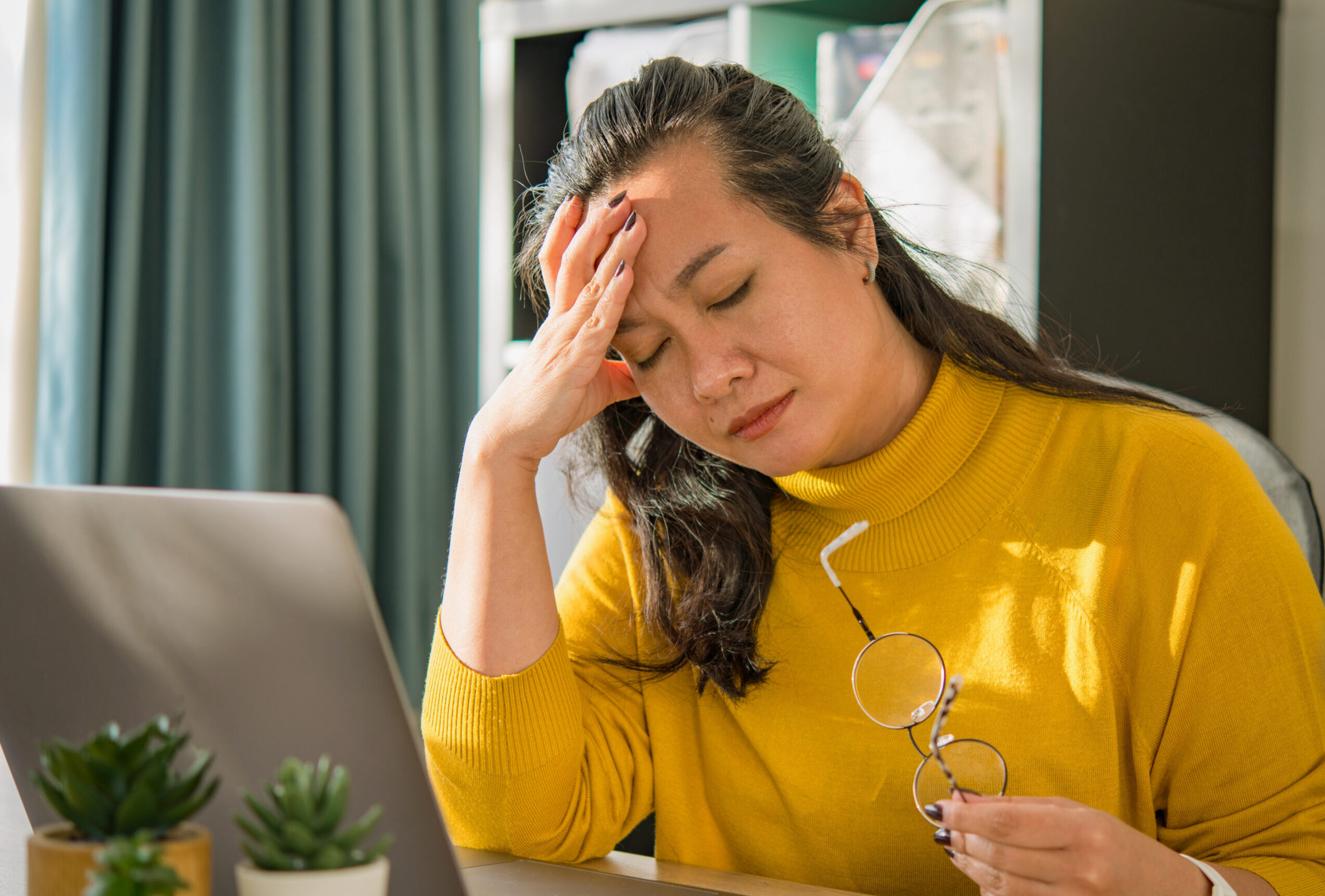 Woman looking stressed with sitting at a desk with an open laptop.