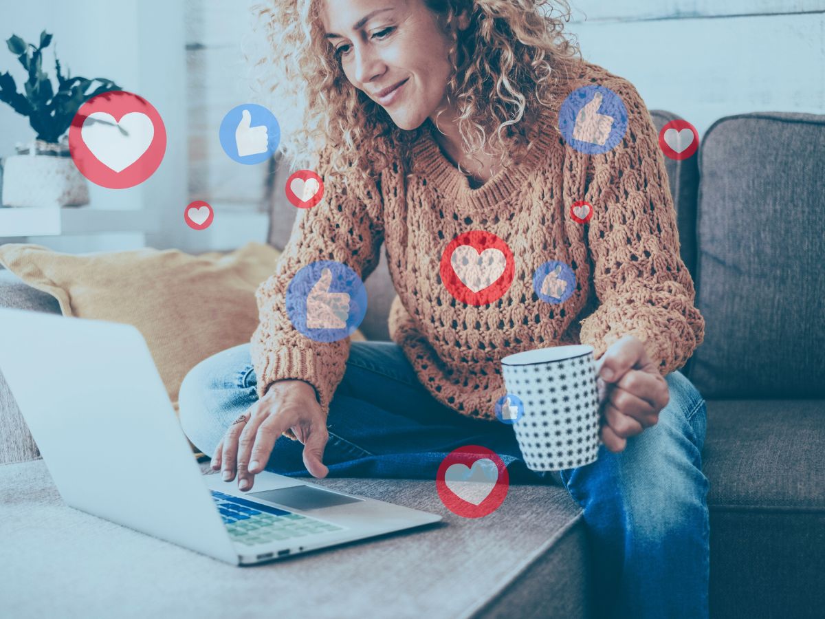 Woman holding coffee mug looking at laptop smiling, social media react graphics around her