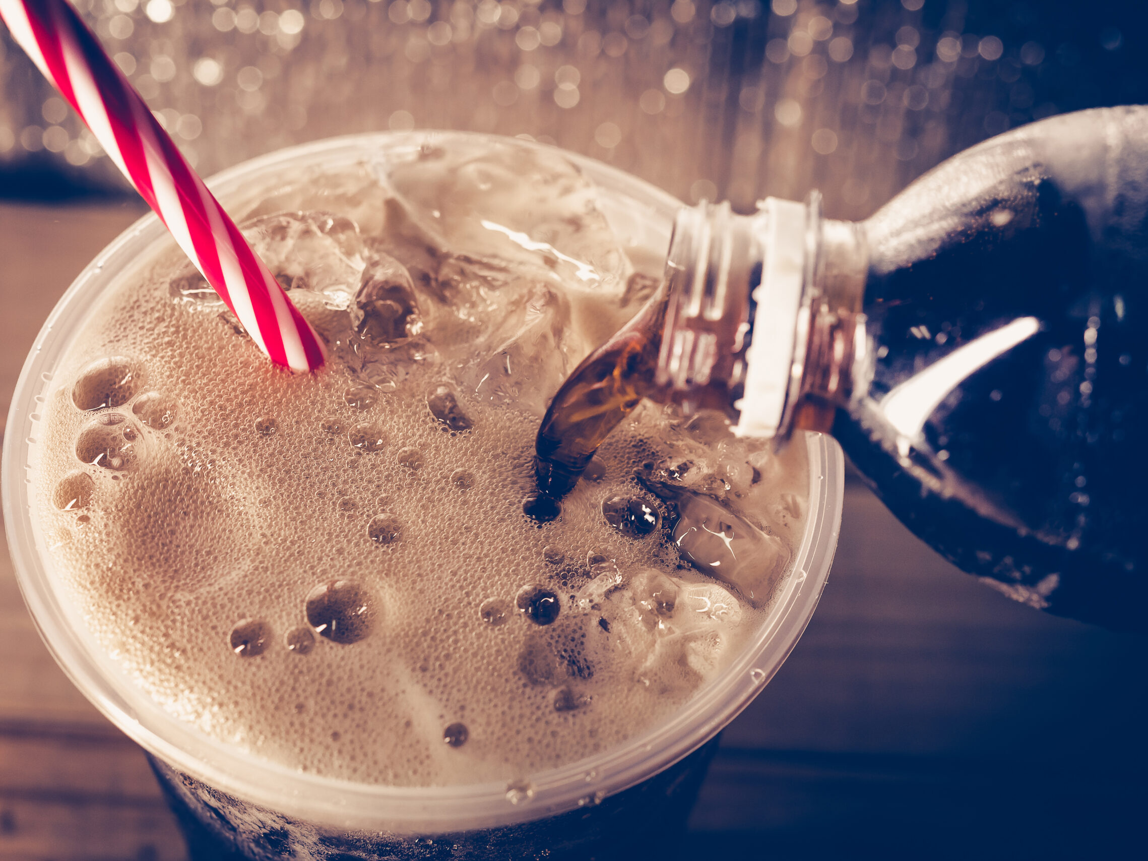 A bottle of cola being poured into a cup with ice