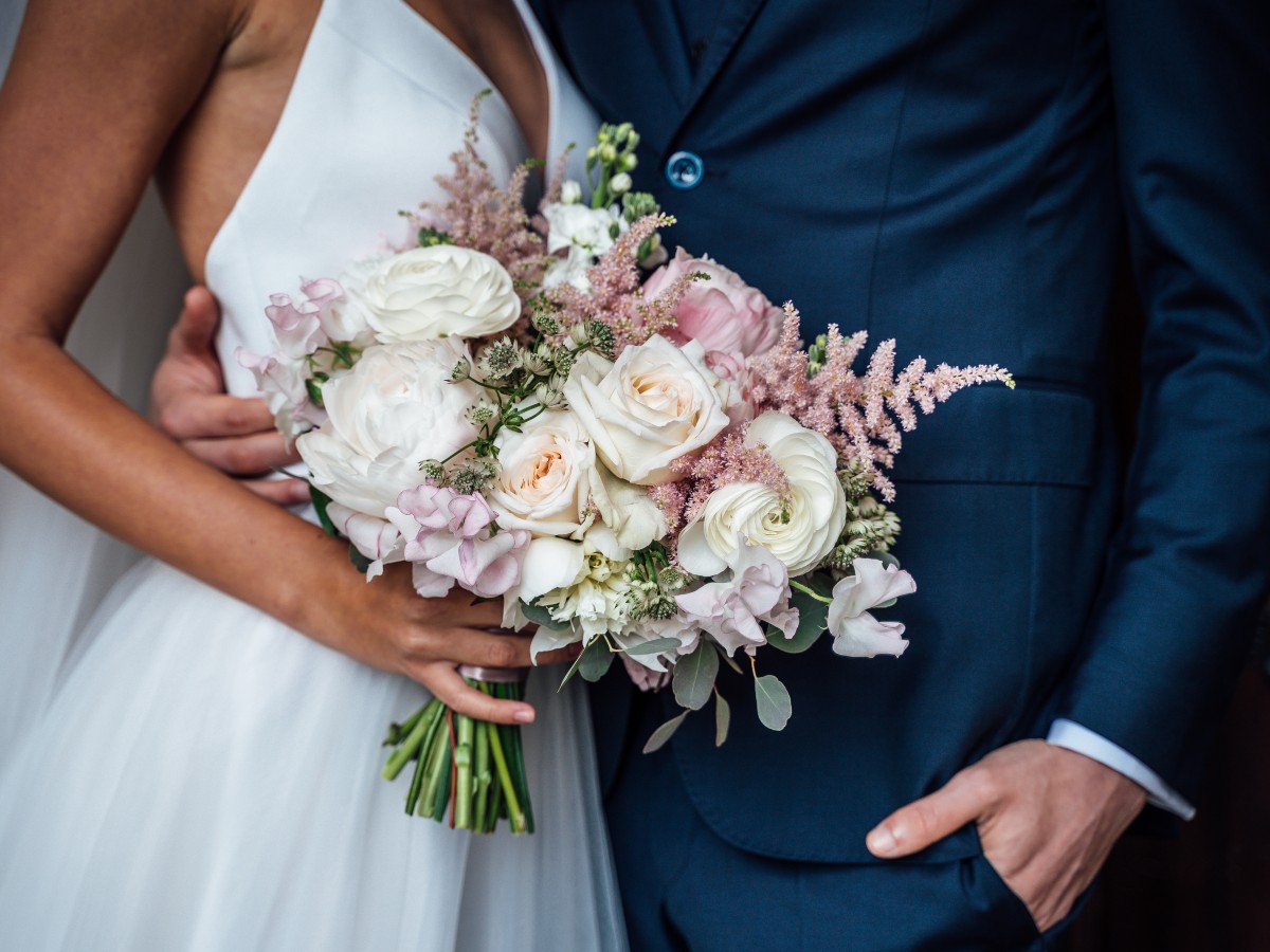 Bride and groom photographed from the shoulders down. Bride is holding a bouquet of flowers