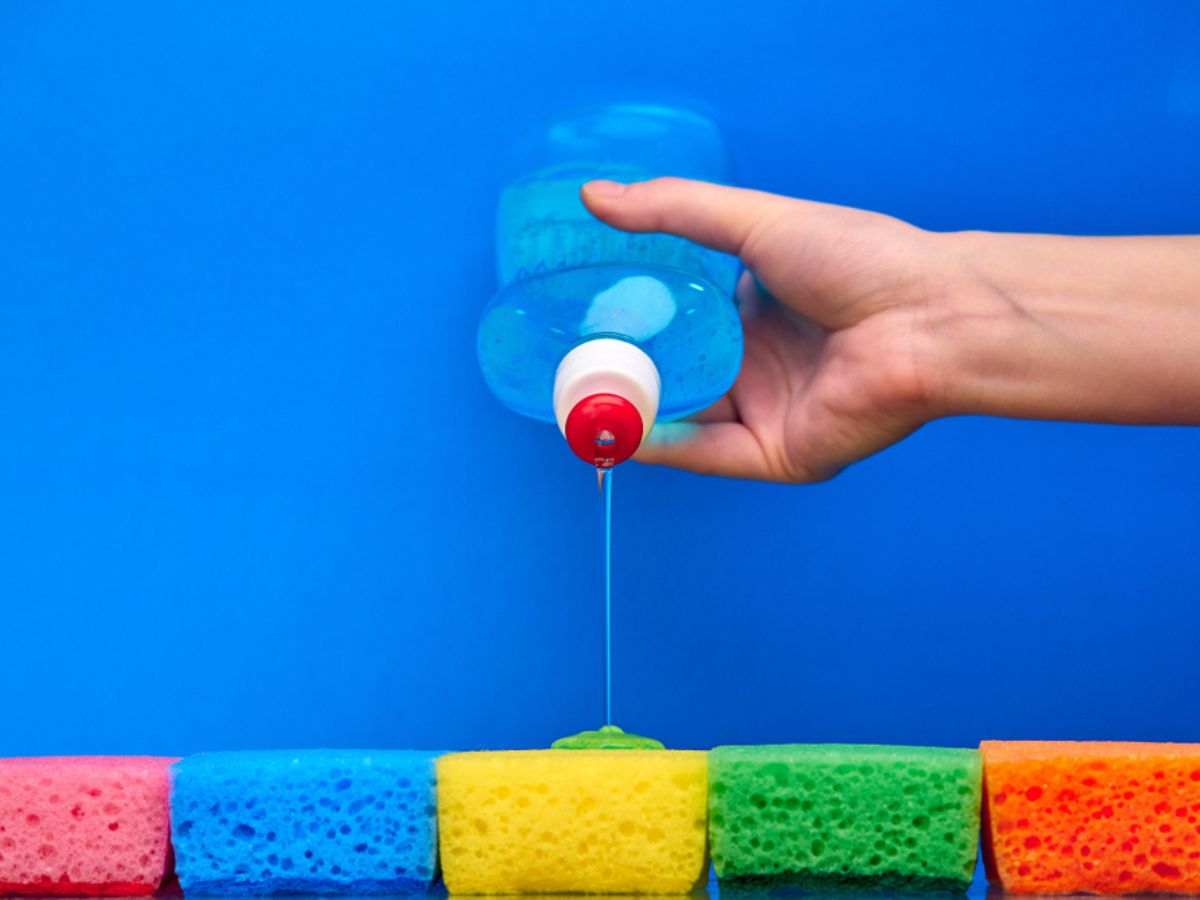 Hand pouring dishwashing liquid onto multicolored sponges