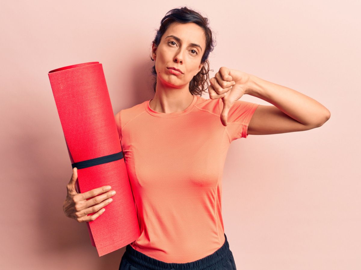 Woman holding a yoga mat with an unhappy expression and thumb down