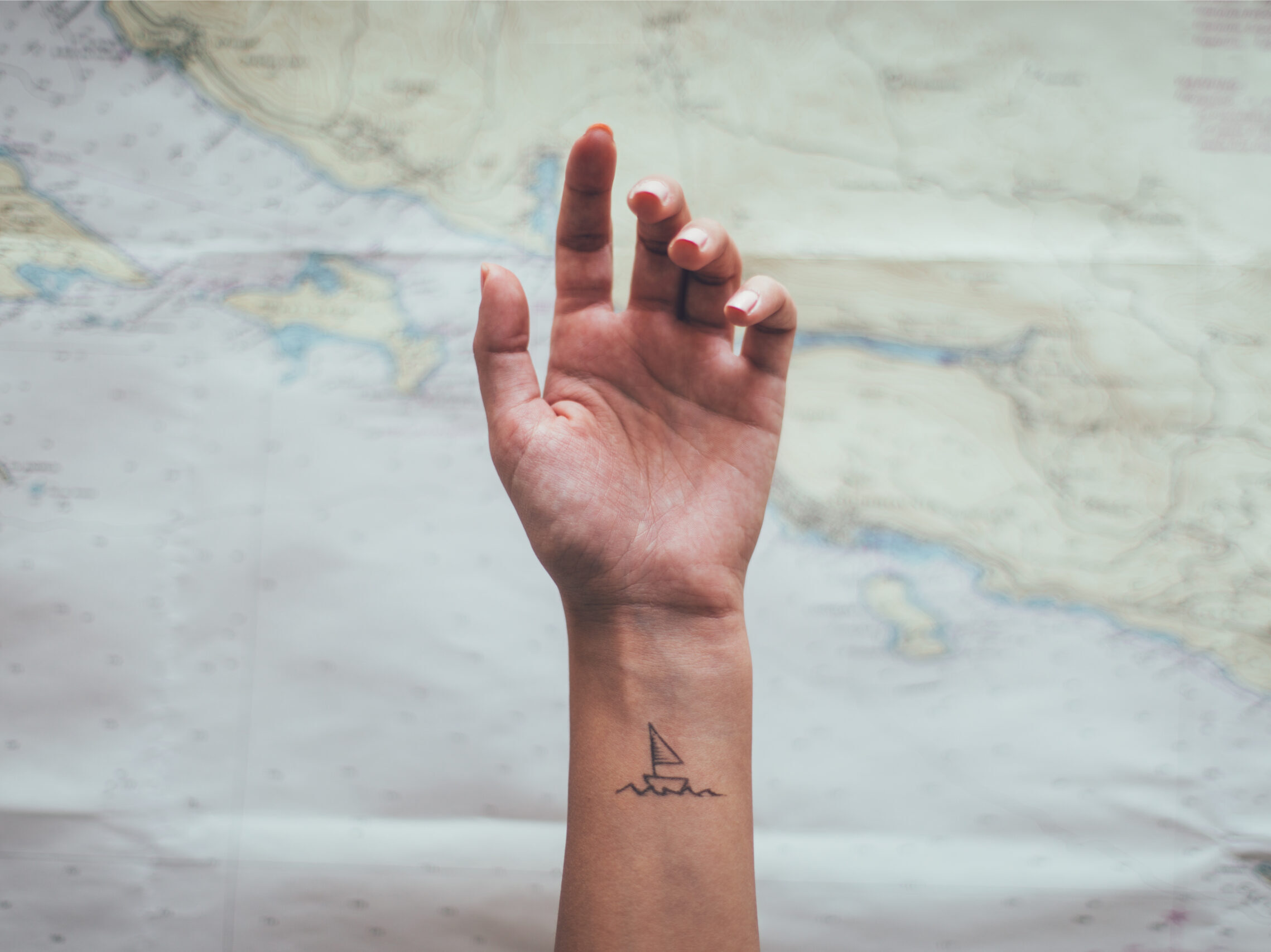 A small simple sailboat tattoo on a woman's wrist