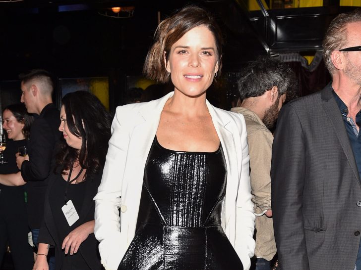 Neve Campbell smiles in black leather top and white blazer