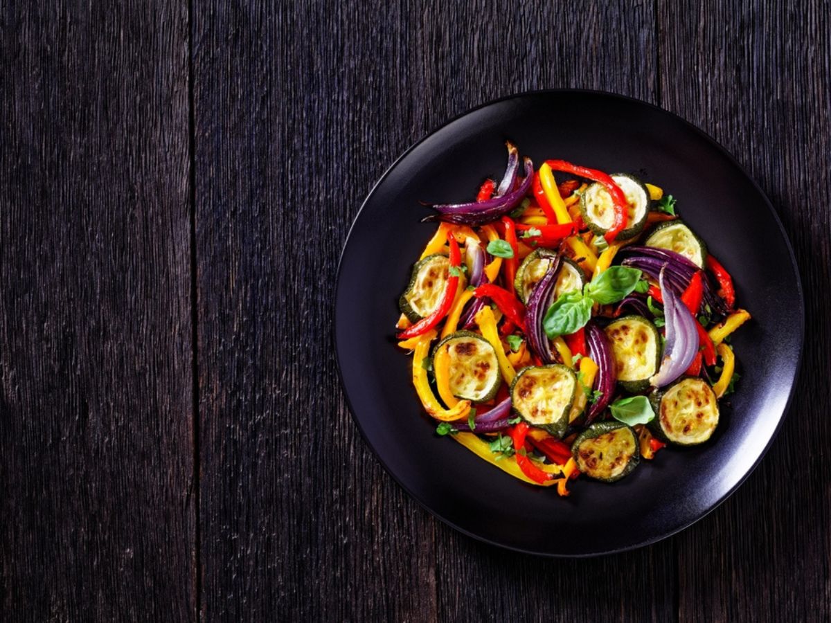 Roasted vegetables sitting on a black plate and dark wood background