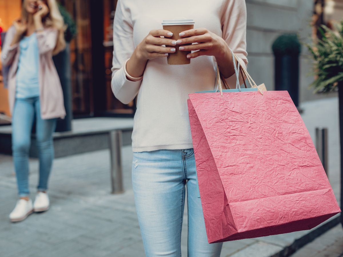 Women holding shopping bags and a cup of coffee with another woman on the phone in the background