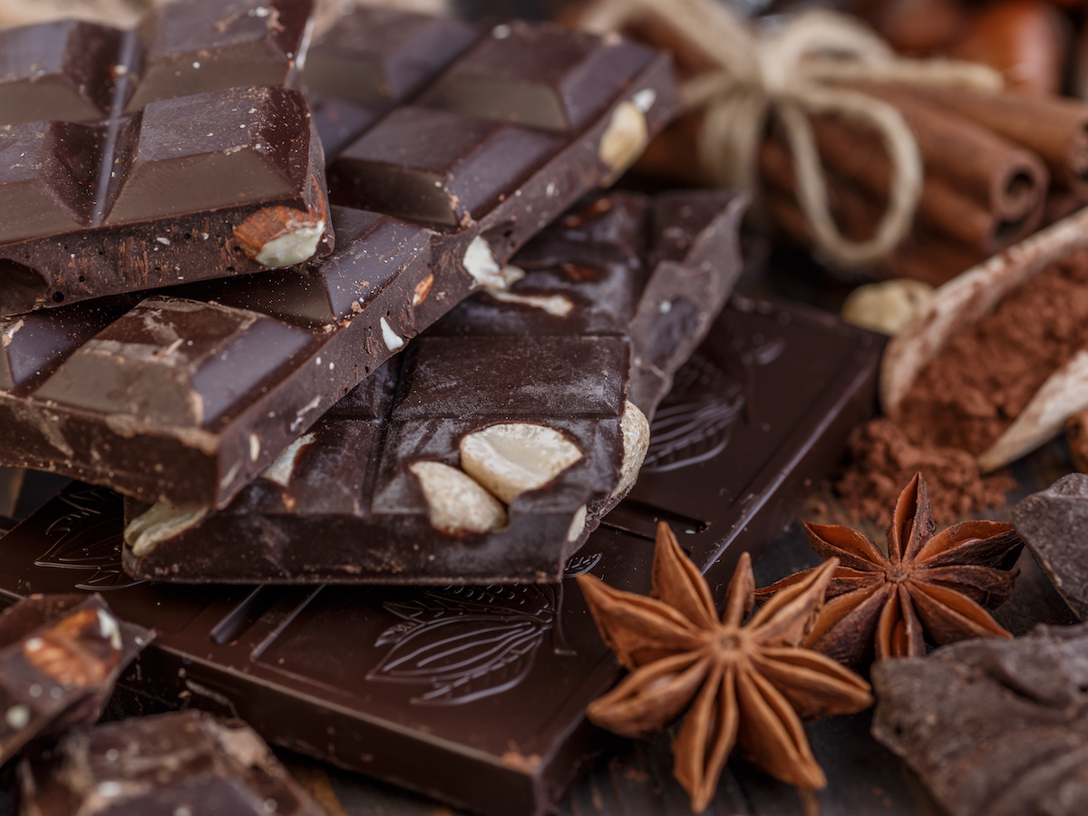 Stack of chocolate bars with pods and nuts on a wooden table