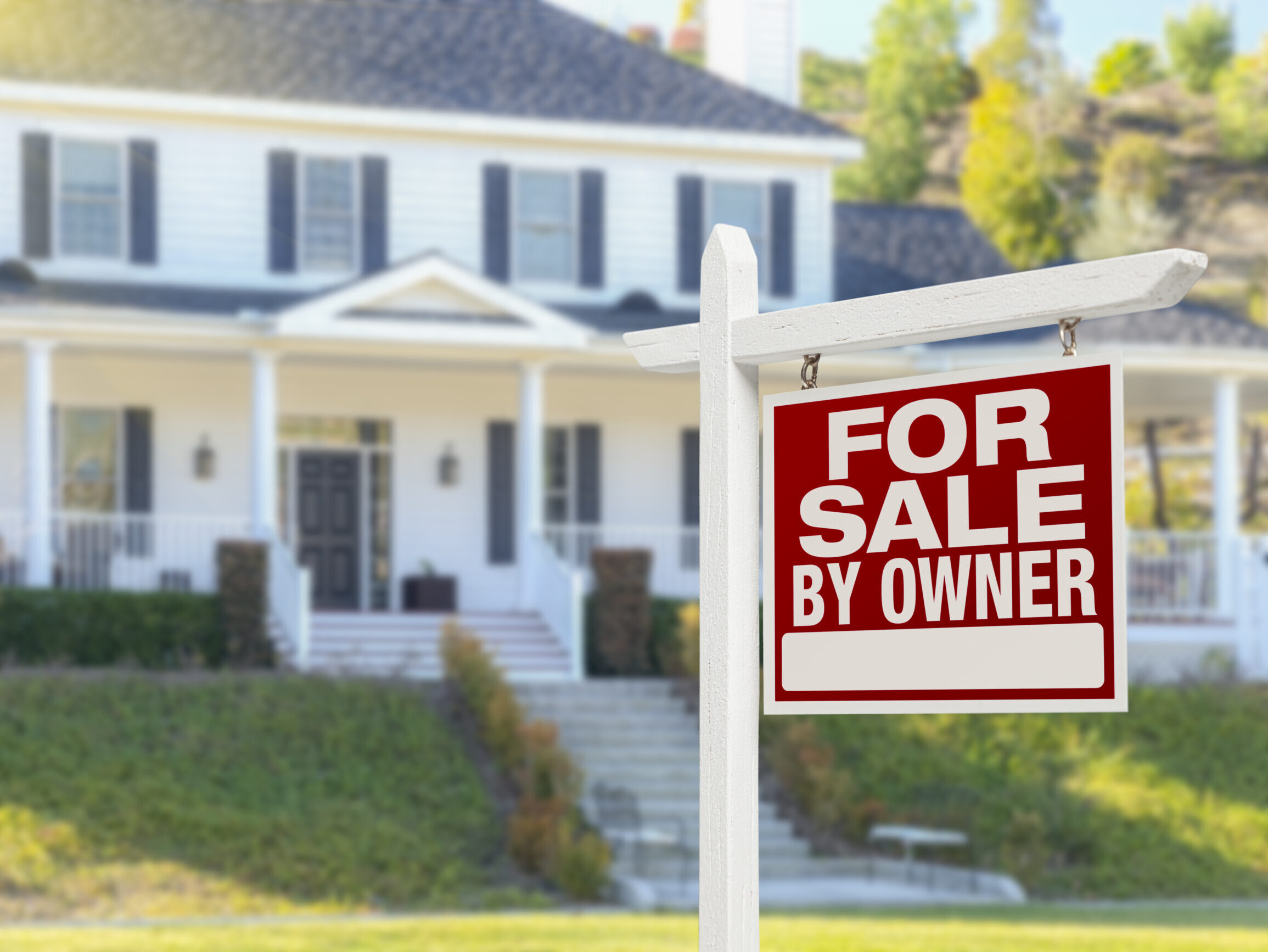 A for sale by owner sign in the front yard of a home