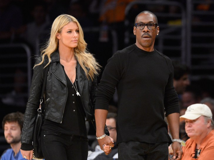 Paige Butcher (L) and Eddie Murphy holding hands at a basketball game dressed in all balck