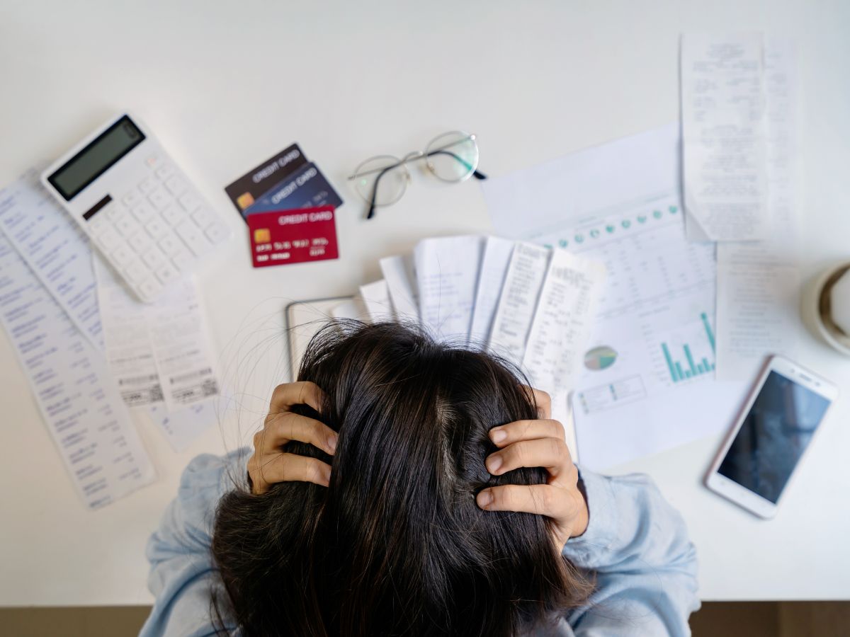 Overhead view of woman with head in hands, stressed about bills in front of her