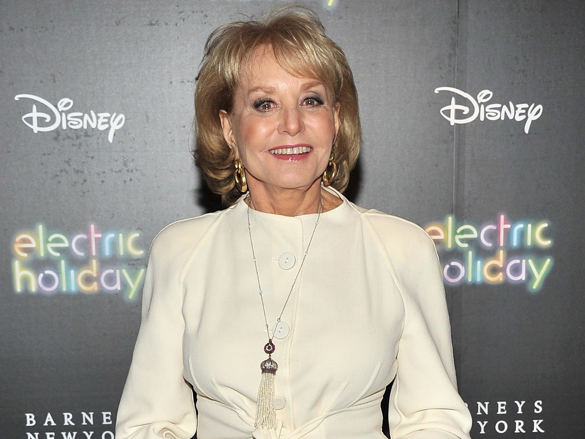 Barbara Walters smiles in off-white dress against gray backdrop