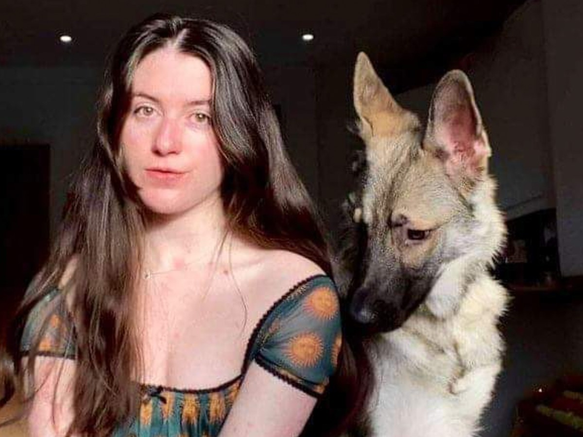 Lucy Beall (L) in patterned dress sitting next to German Shepherd dog