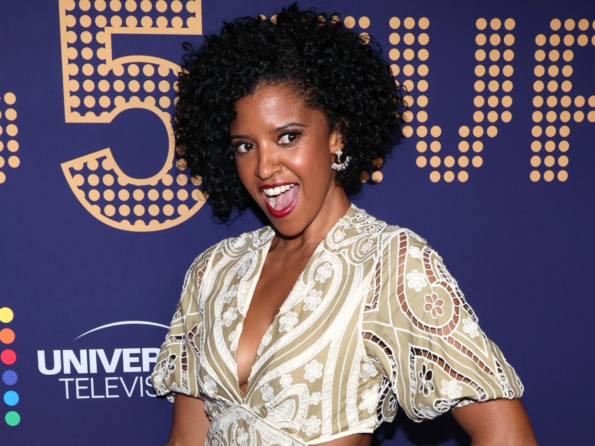 Renée Elise Goldsberry smiles in patterned dress against purple backdrop