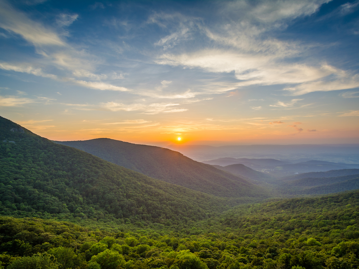 the sun setting over mountains covered in trees