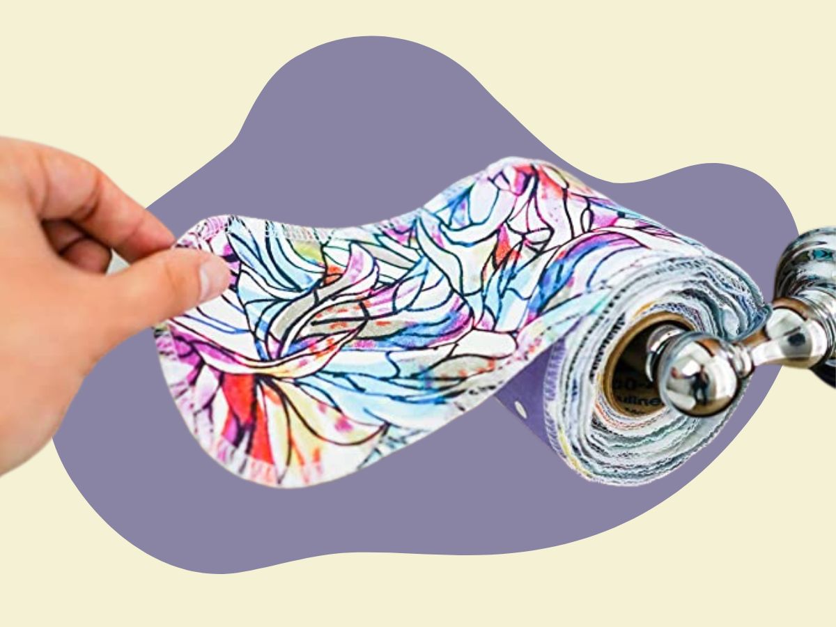 Hand pulling off a "sheet" of reusable toilet paper on a purple-and-cream background