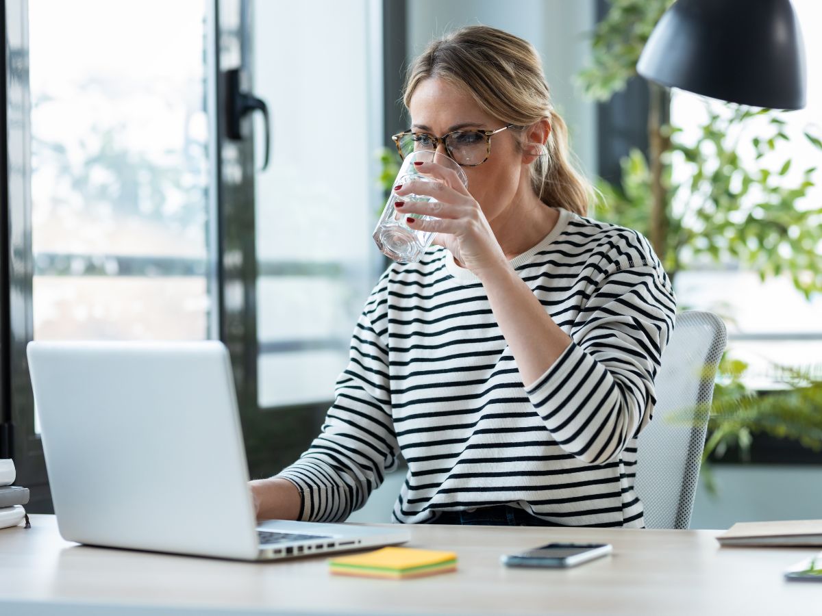 Woman drinking water while working at her laptop computer