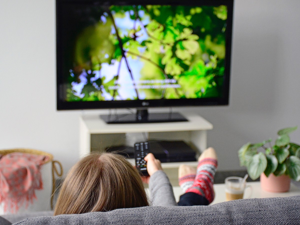 Image of woman on couch pointing remote at television